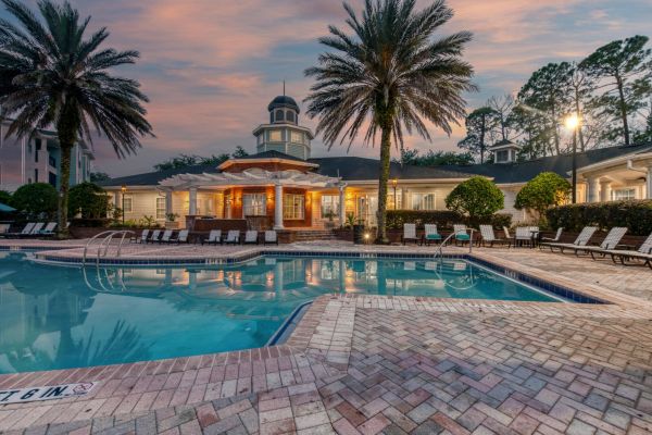 Integra Landing Resort-style pool with lounge chairs, palm trees, and a clubhouse at sunset.