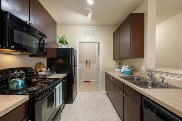 Integra Woods Modern kitchen with dark cabinets, black appliances, double sink, and beige countertops, well-lit and tidy.