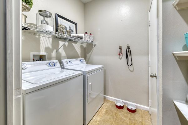 Integra Landing Laundry room with washer and dryer, wall shelves, pet bowls, and laundry supplies on a wire shelf above.
