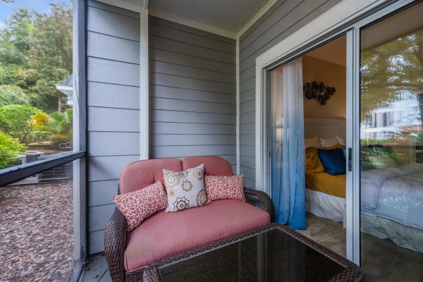 Integra Woods Wicker loveseat with cushions on a screened porch, next to a sliding door leading to a cozy bedroom.