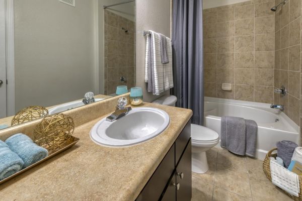 Integra Landing Modern bathroom with beige countertop, sink, towels, and a bathtub with tan tile and a gray shower curtain.