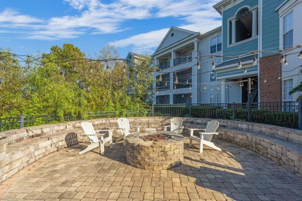 Integra Landing Curved stone patio with a fire pit, Adirondack chairs, string lights, and apartment buildings in the background.