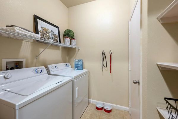 Integra Landing Laundry room with washer, dryer, shelf with decor, pet leashes on wall, and two pet bowls on the floor.