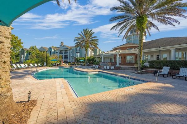 Integra Landing Outdoor swimming pool with lounge chairs, palm trees, and residential buildings under a blue sky.