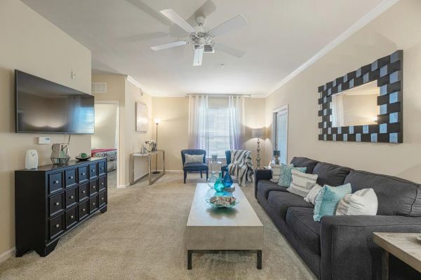 Integra Woods Neutral living room with gray sofa, coffee table, TV, dresser, mirror, chairs, and large window with curtains.