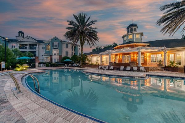 Integra Landing Resort-style pool with lounge chairs, palm trees, and a large building at sunset.