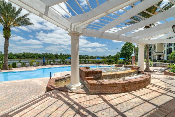 Integra Landing Outdoor pool with brick hot tub under a white pergola, palm trees, and lake in the background.