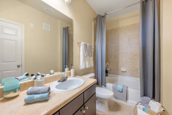 Integra Woods Modern bathroom with a sink, mirror, toilet, bathtub, and gray towels neatly arranged on the counter and racks.