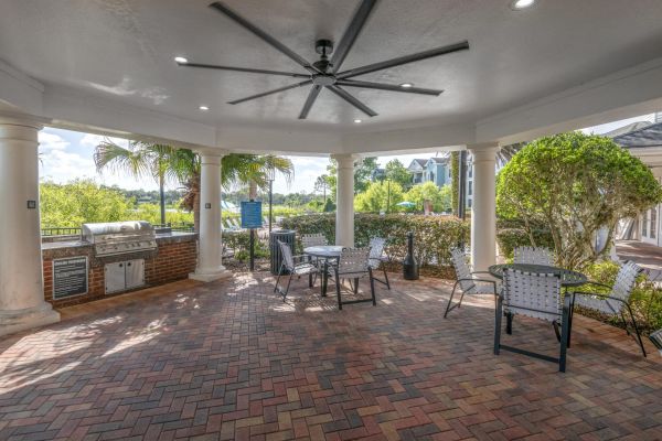 Integra Landing Covered patio with ceiling fan, grill, and patio tables overlooking lush greenery and trees.