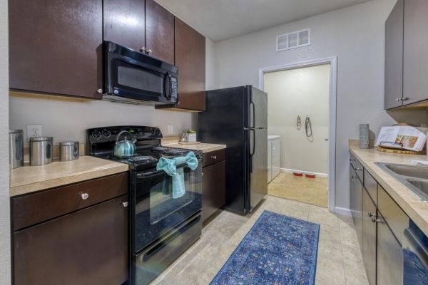 Integra Landing Modern kitchen with dark cabinets, black appliances, blue rug, and a kettle on the stove.