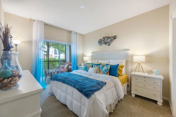 Integra Woods Bright bedroom with a large bed, blue accents, white furniture, and sliding glass doors to a patio.